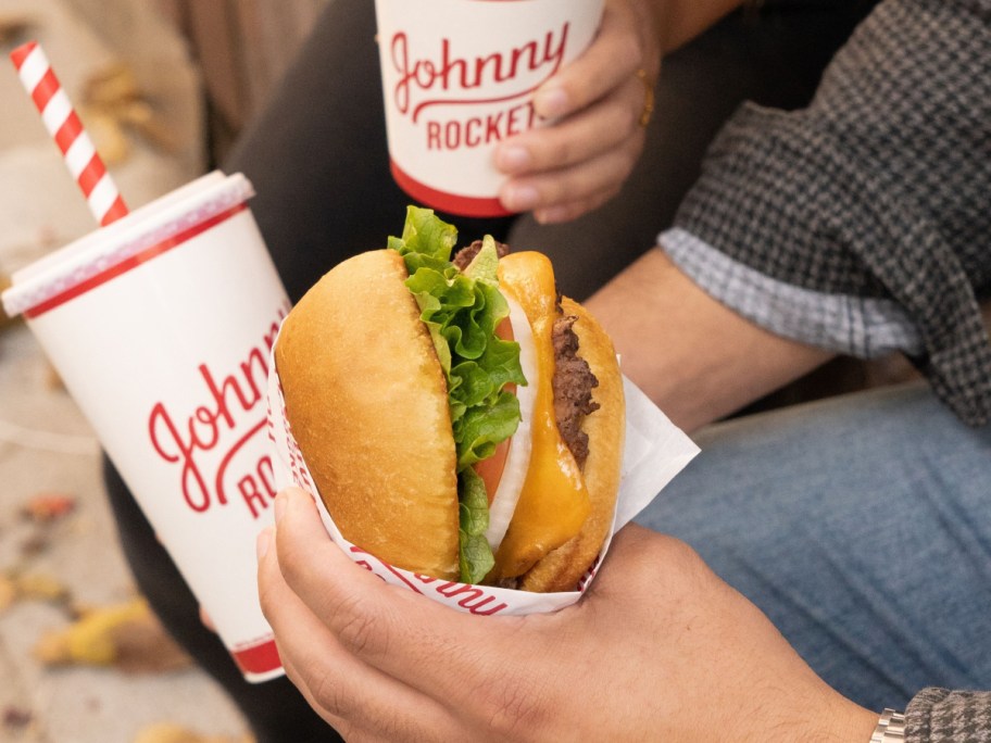 holding a burger and a drink from Johnny Rockets