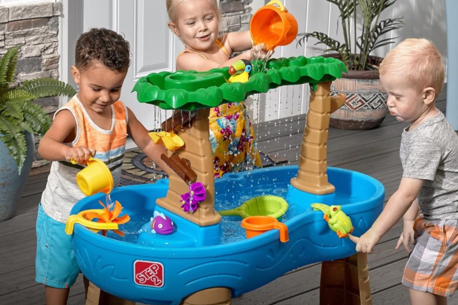 three toddlers standing around rain forest themed water table