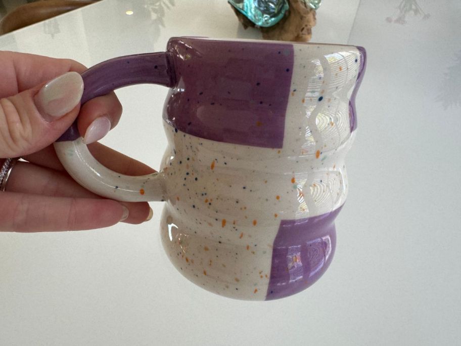 a woman's hand holding a purple and white coffee mug