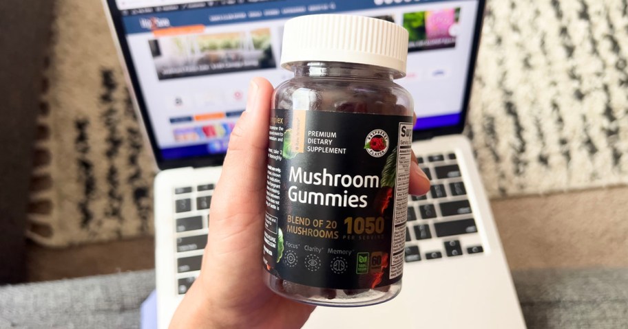 hand holding mushroom gummies bottle above laptop