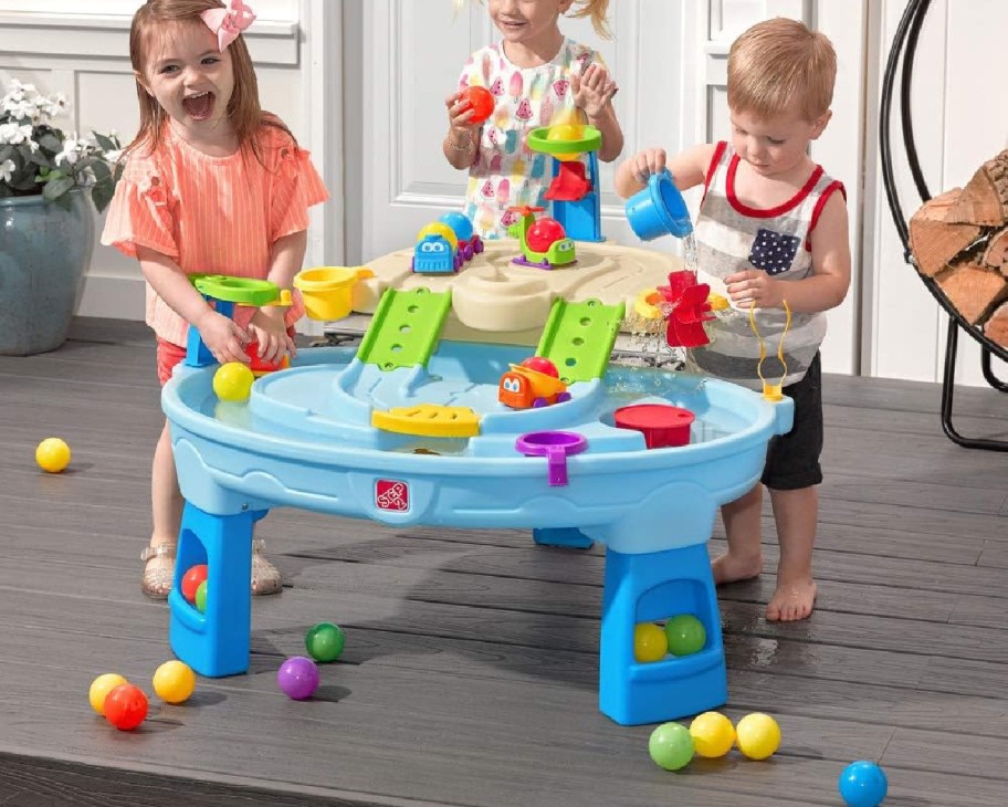 three toddlers near water table with balls on ground