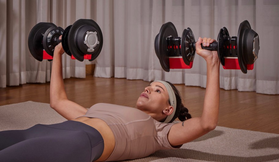 woman laying down in tan shirt holding two dumbbells