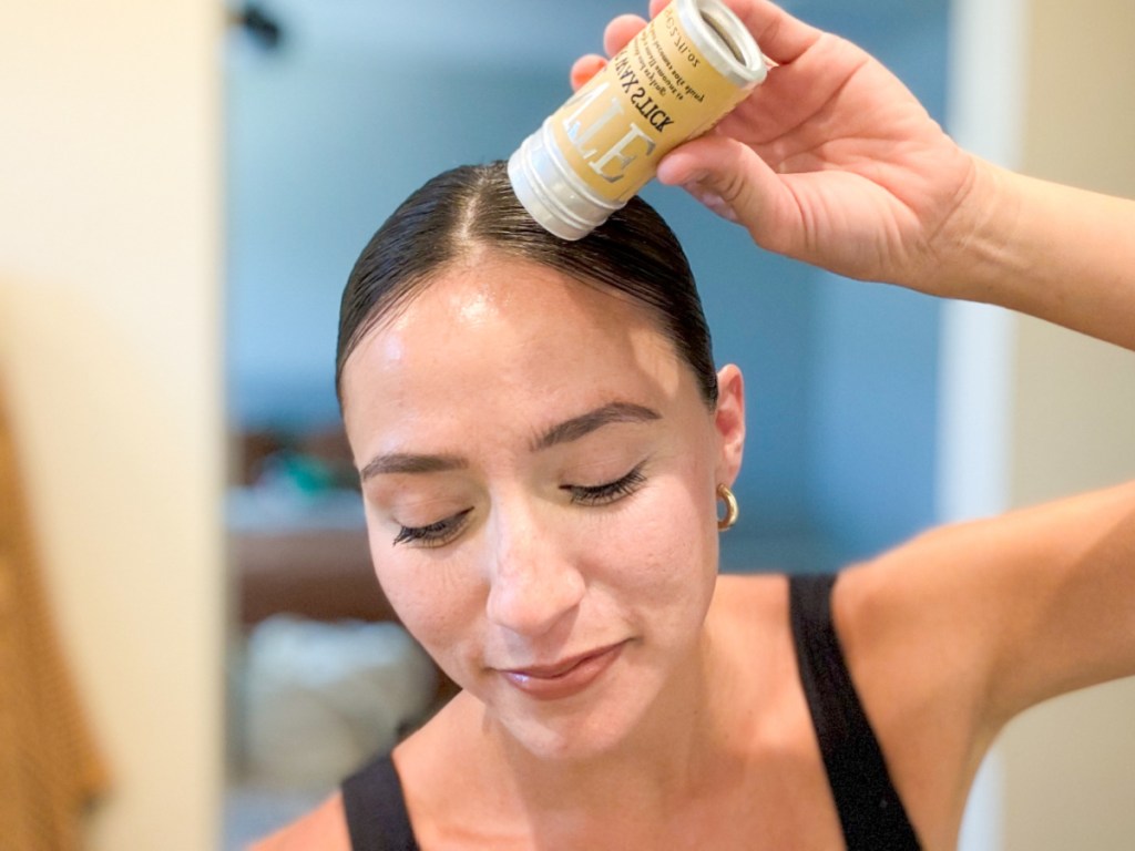 woman applying hair wax stick to top of scalp