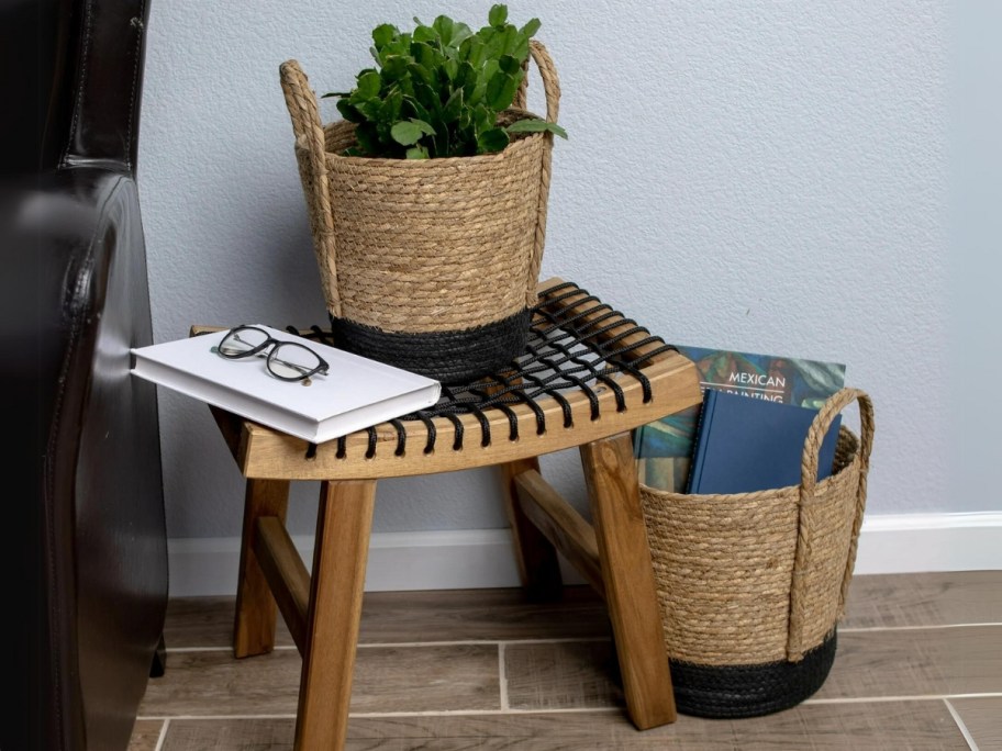 small and medium size tan and black seagrass storage baskets with items in them, one on a small stool, the other in the floor