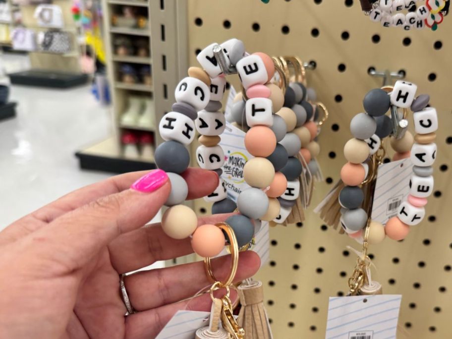 hand holding a Making The Grade Teach Silicone Bracelet Keychain thats on display at the store