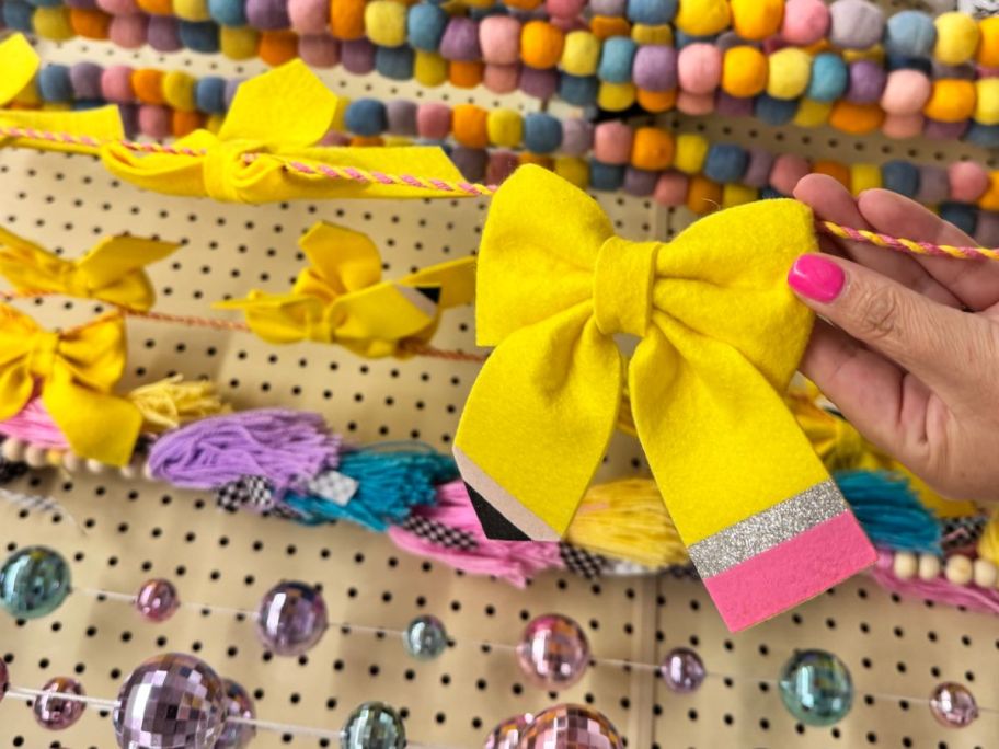 hand holding Making The Grade Yellow Pencil Bow Garland at the store