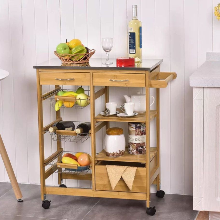 a natural wood colored rolling kitchen cart shown with kitchenware