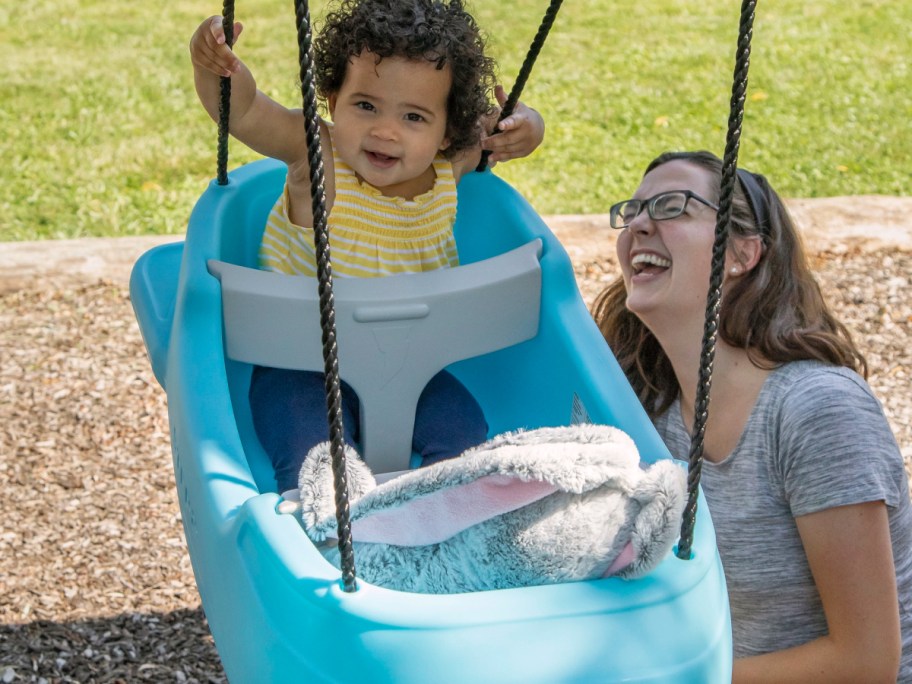 toddler and a plush rabbit in a Step2 Swing with a woman off to the side looking on