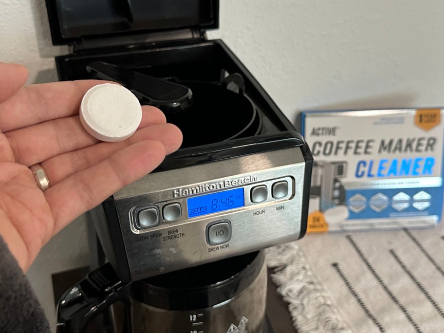 hand holding coffee maker cleaner above coffee maker