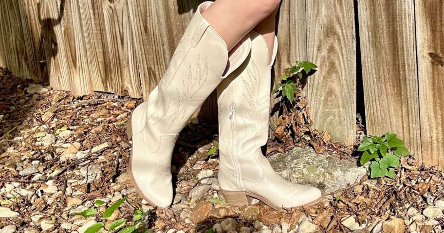 woman wearing cream colored No Boundaries Women's Tall Western Boots in front of fence