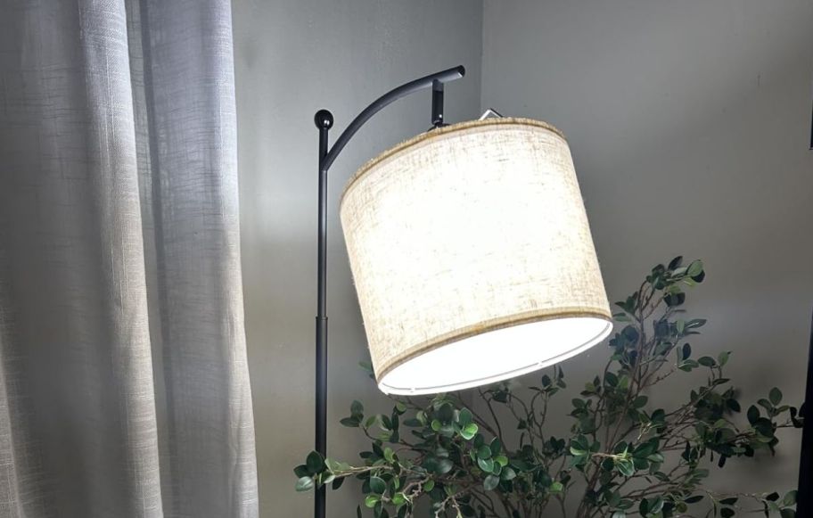 a lit black iron floor lamp with round shade 