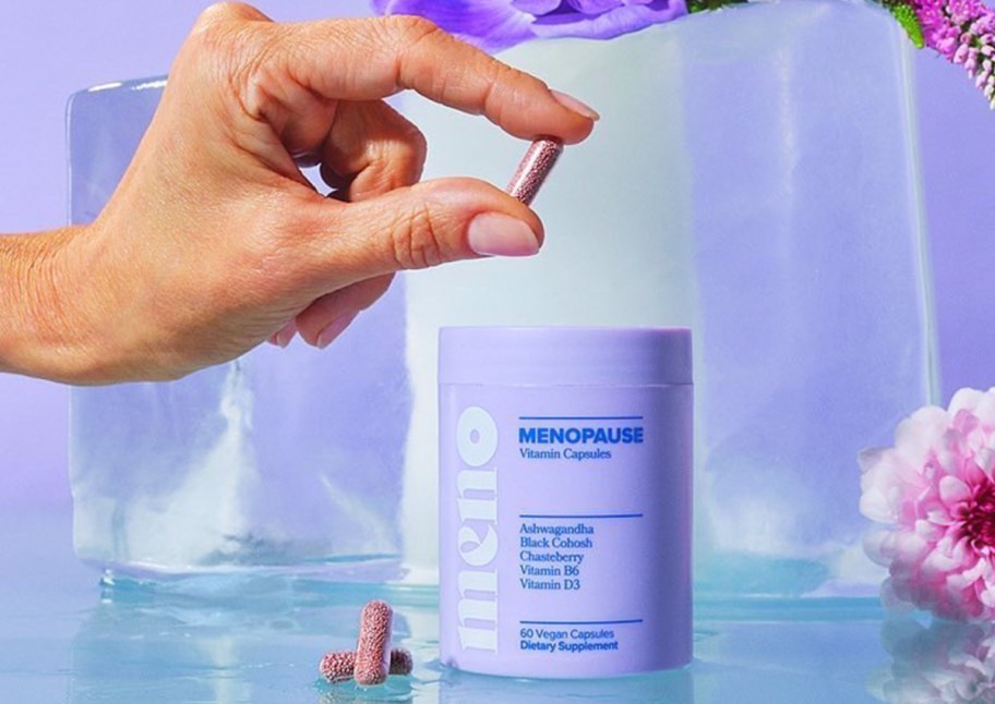 fingers holding purple menopause supplement capsule over jar