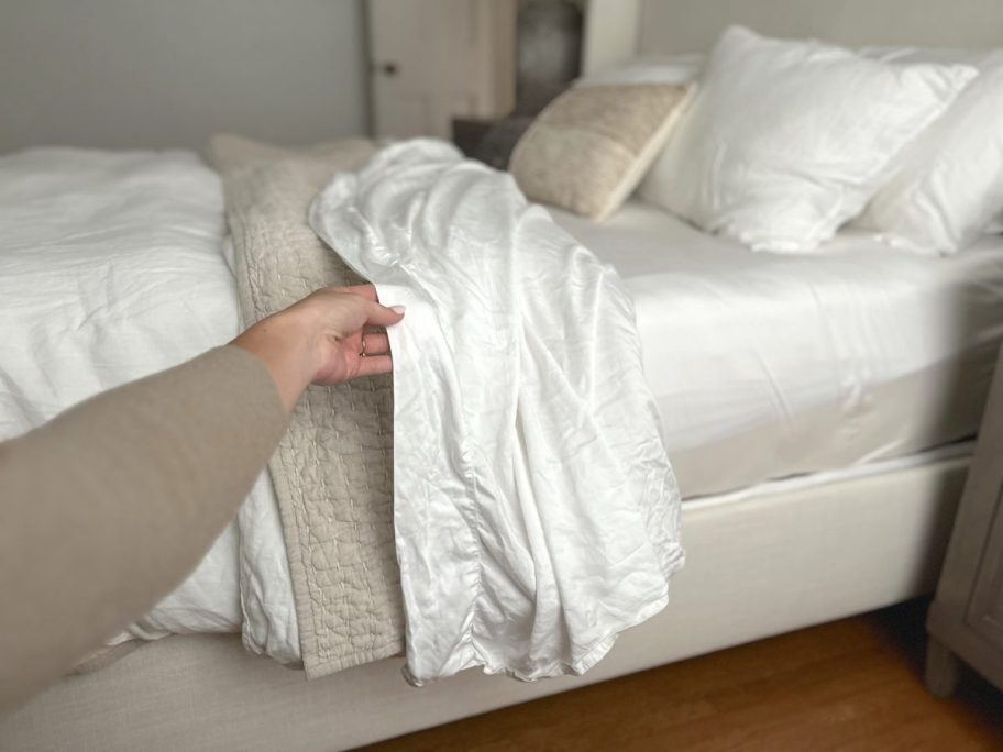 hand holding side of white sheet hanging down side of bed