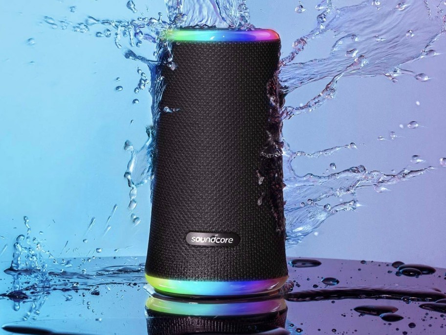 portable speaker with lights on table with water splashing on it 