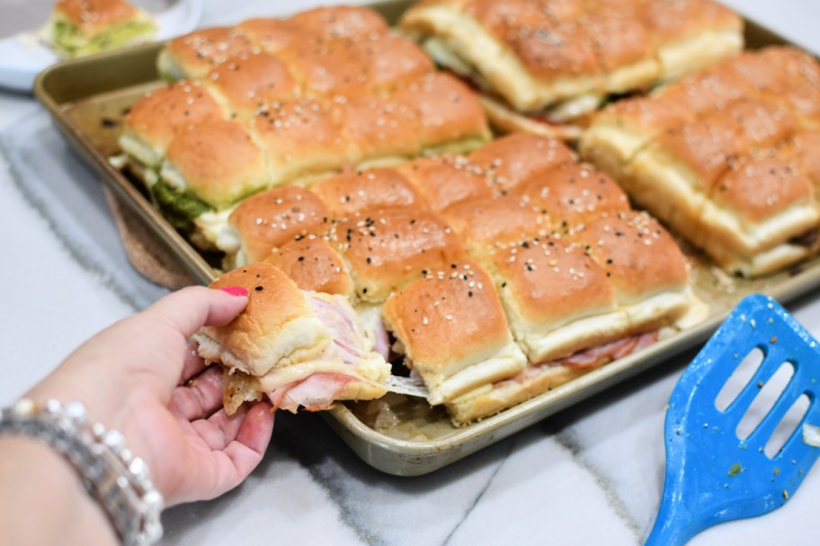 woman picking up a ham and cheese slider sandwich