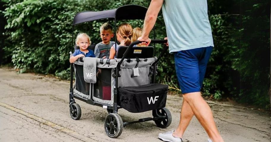 man pushing Wonderfold W4 Quad Stroller Wagon bundled with the Snack Tray, Drink Holder & Mat with kids in it