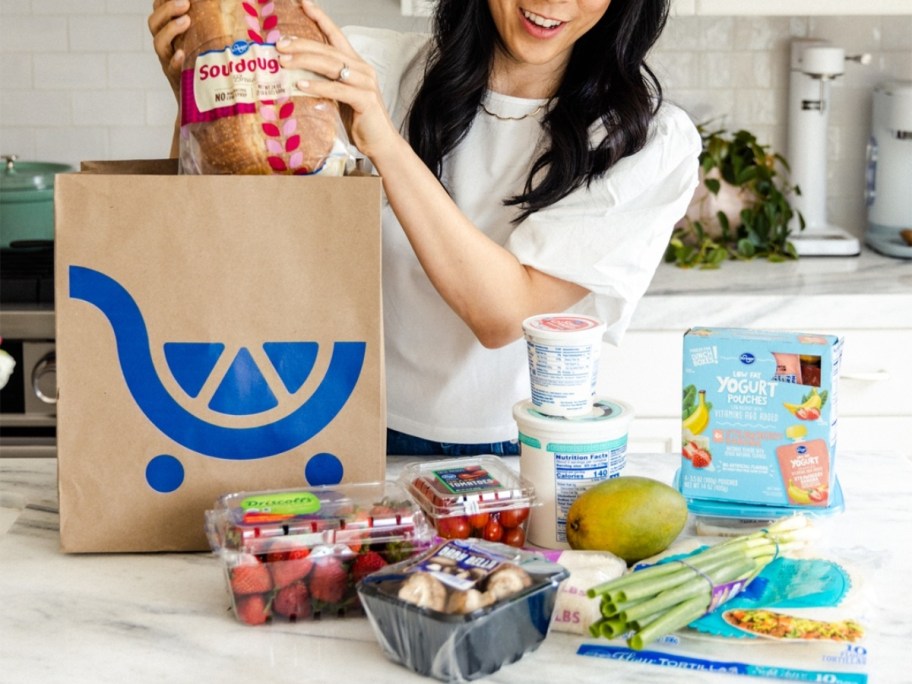 woman holding a Kroger grocery bag standing outside a blue door