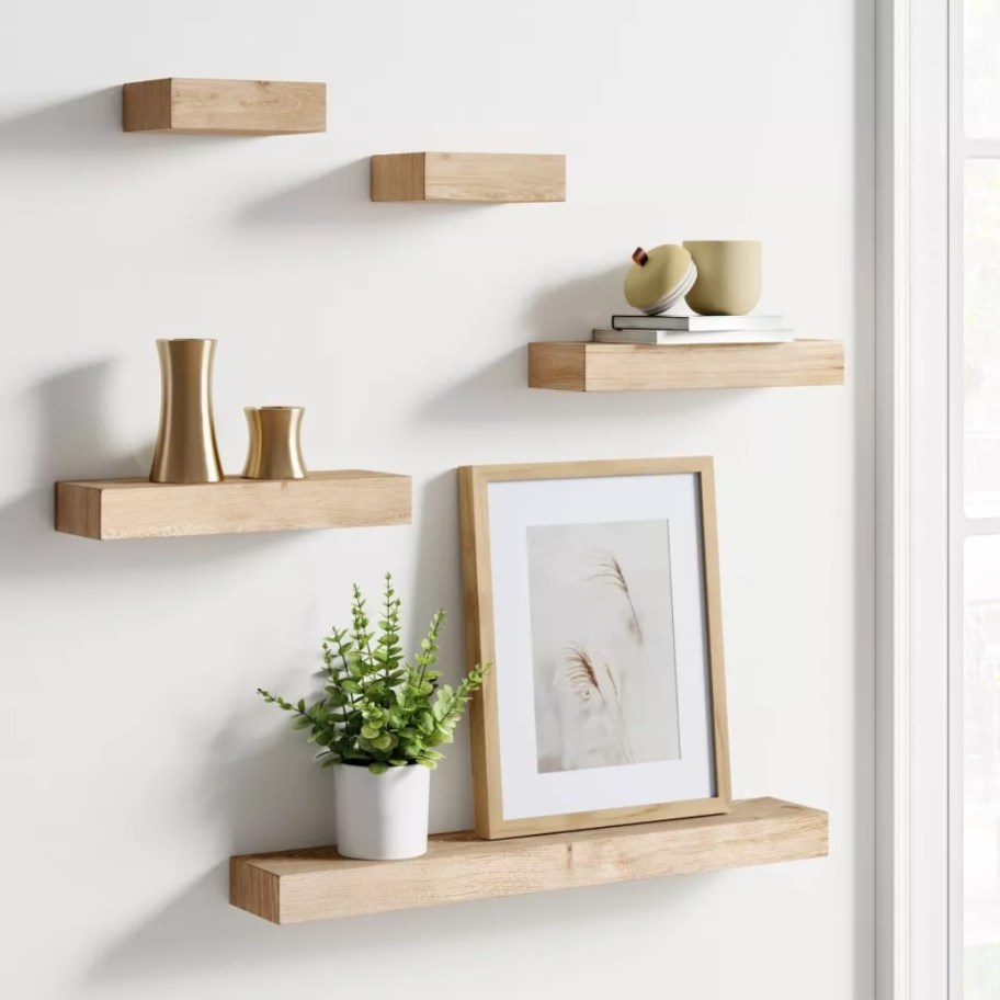 five natural color wood floating shelves in different sizes on a wall with decor on them
