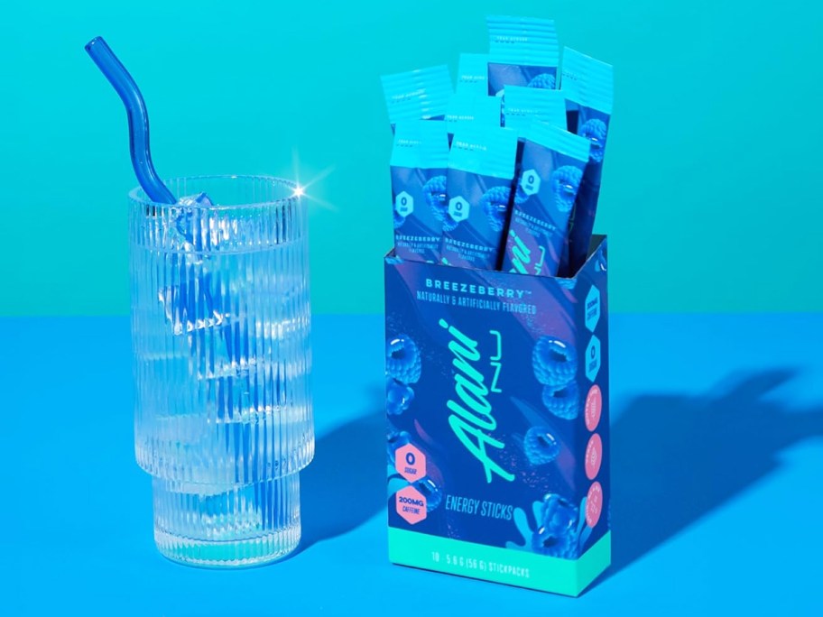 blue box of Alani Nu Energy Powder Sticks next to a glass of water