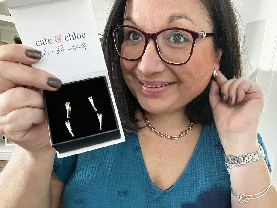 woman holding up a box of earrings and touching the same earrings in her ear