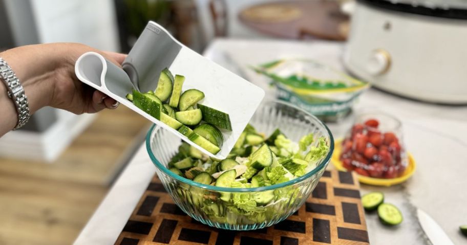 woman using Dandy Folding Cutting Board Scraper to put cucumbers into bowl