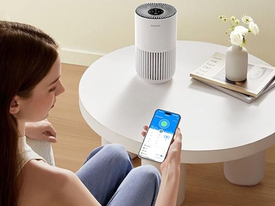 woman looking at her phone in front of an air purifier