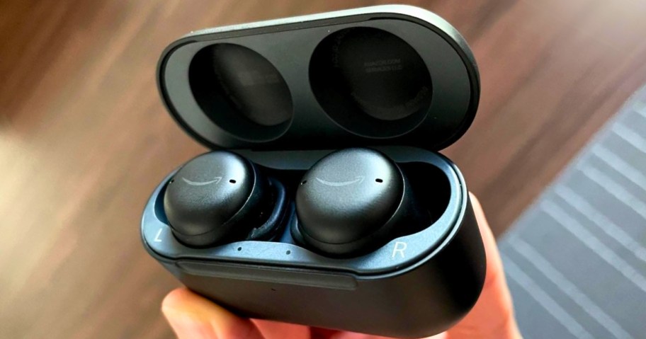 hand holding a pair of Black Amazon Echo Buds earbuds in a charging case