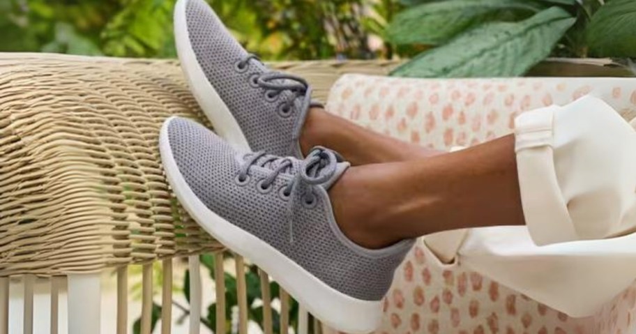 woman's feet up on the end of a rattan outdoor chair wearing grey and white allbirds sneakers