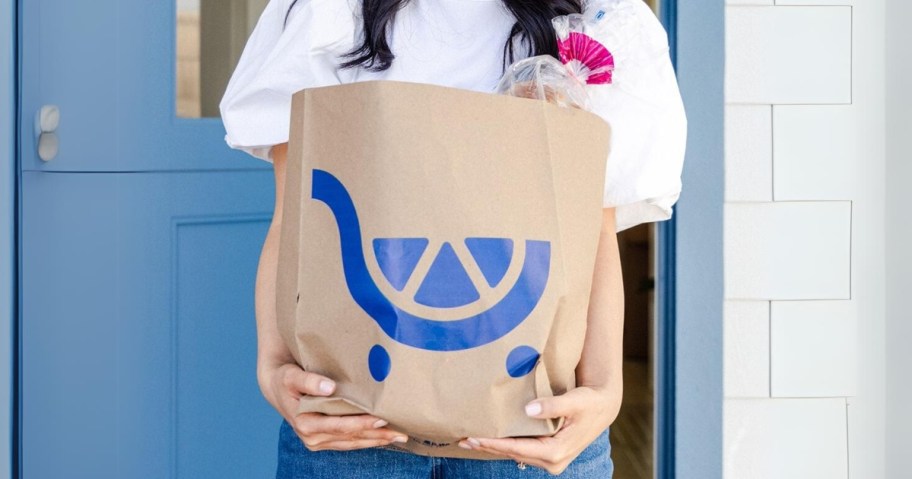 woman holding a Kroger grocery bag standing outside a blue door