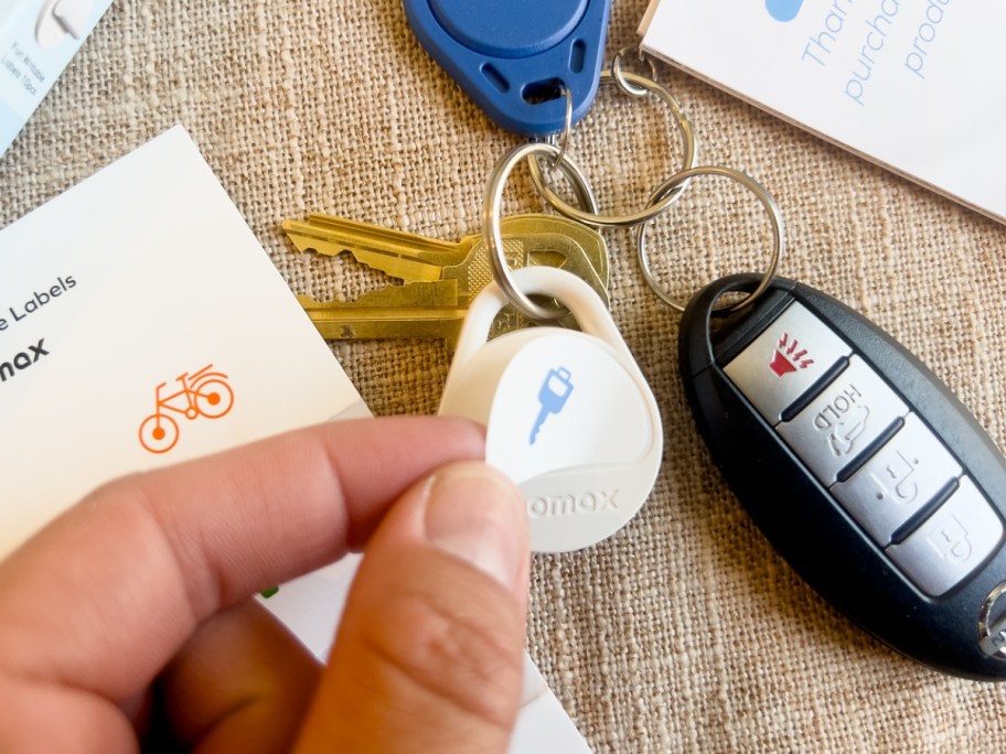 hand putting a sticker on a white tracker tag on a keychain