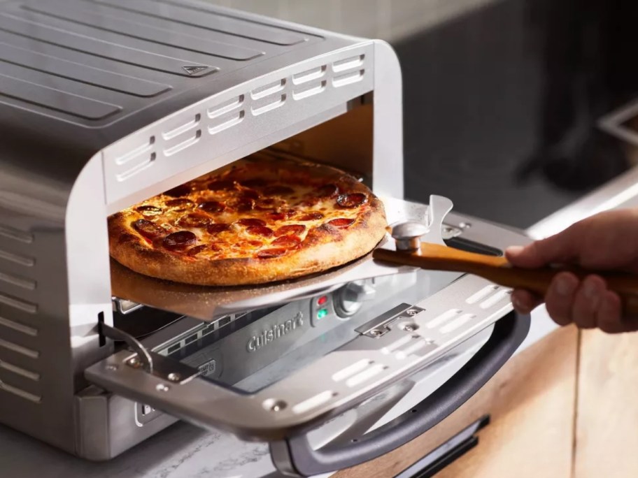 person pulling a fresh baked pizza out of a stainless steel indoor pizza oven