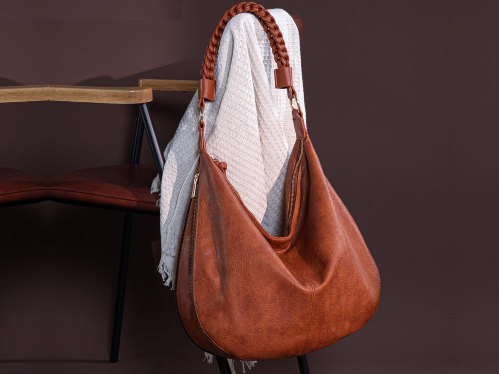 Brown leather Montana West hobo bag hanging on back of chair on top of white sweater