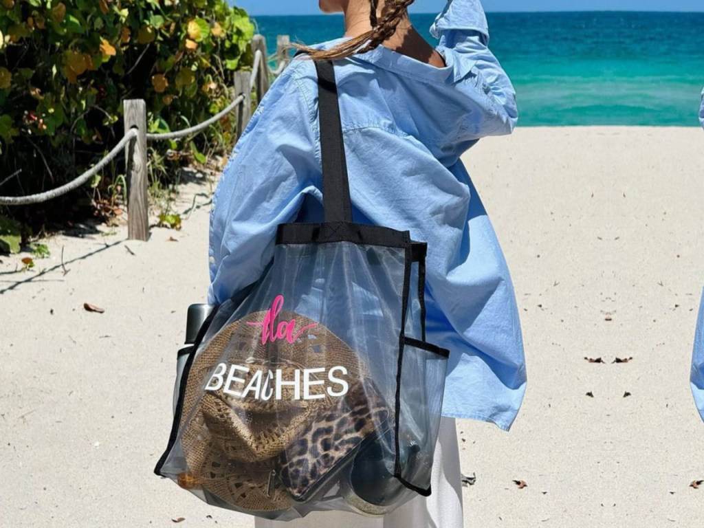 Women carrying Montana West mesh bag filled with apparel and beach items while walking on sand in front of ocean