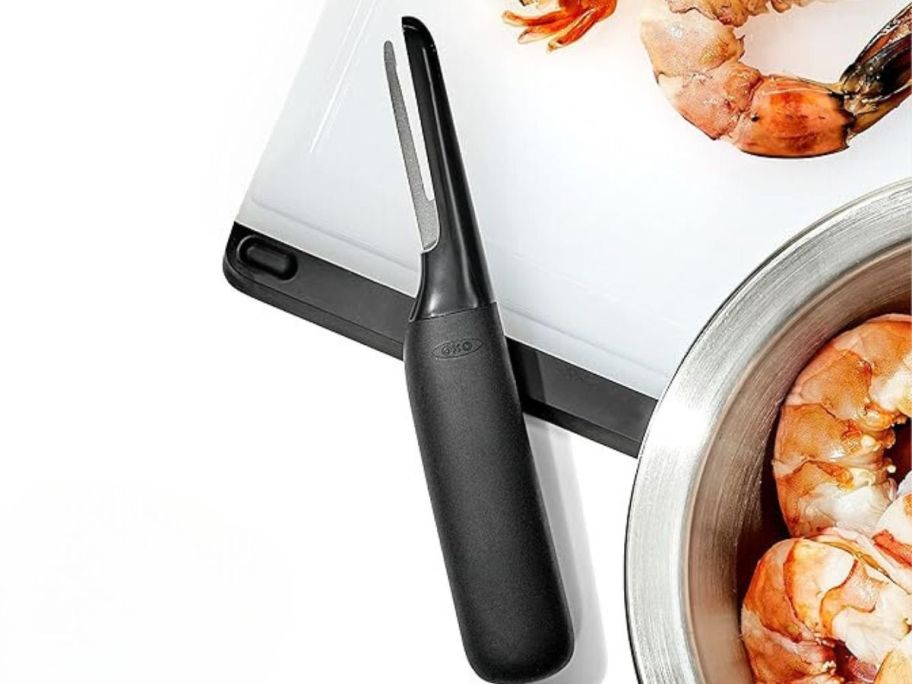 OXO Good Grips Shrimp Deveiner sitting on cutting board next to shrimp