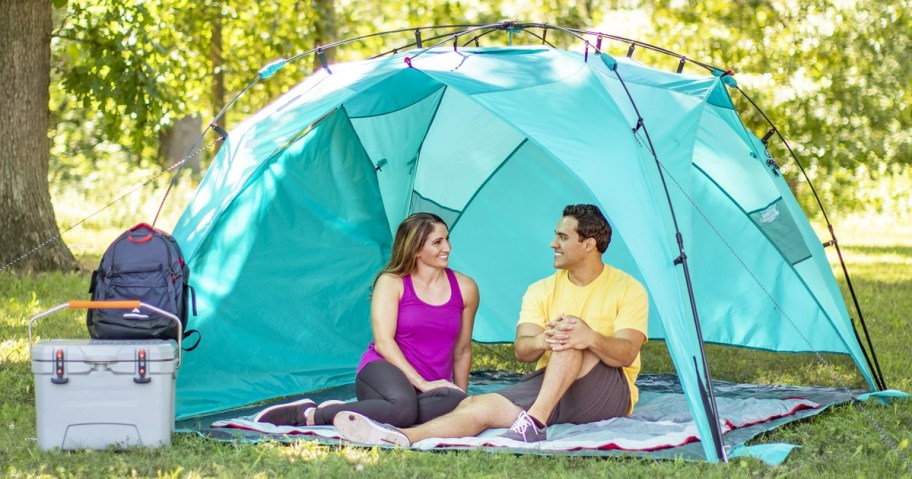 two people sitting under a blue shade tent