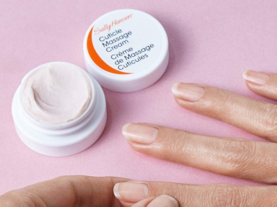 Sally Hansen Cuticle Massage Cream container open, person's hands rubbing the cream into a finger cuticle