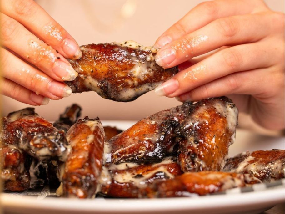 woman's hand holding a Smokey Bones chicken wing over a plate of wings