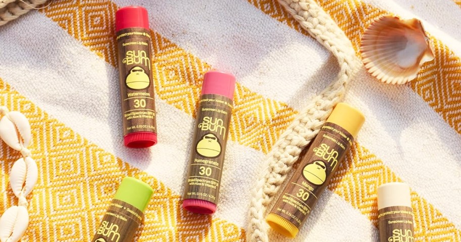 various sun bum lip balms laying on striped beach towel