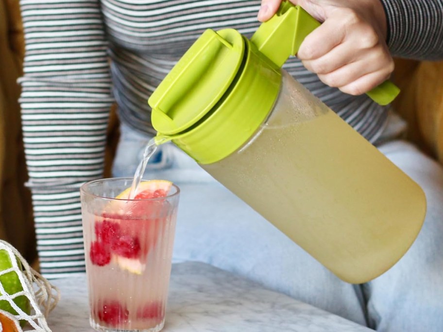 pouring lemonade from a pitcher into glass with fruit pieces