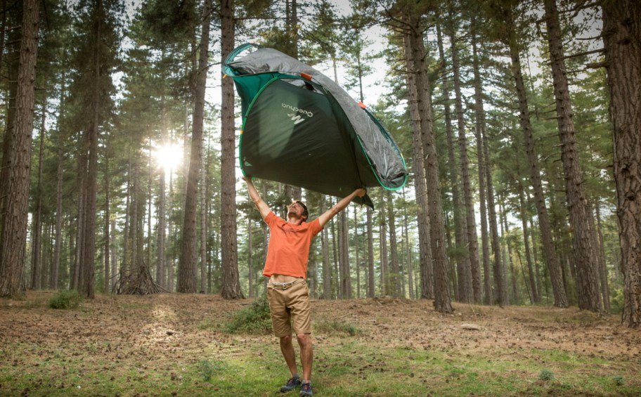 Man lifting a pop up tent over his head in the woods