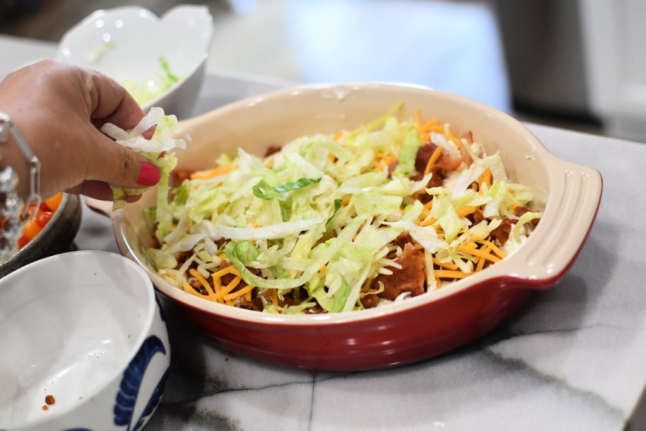 adding cheese and shredded lettuce to blt dip 