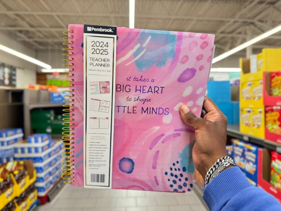 hand holding a teacher planner with pink, purple, and blue retro designs