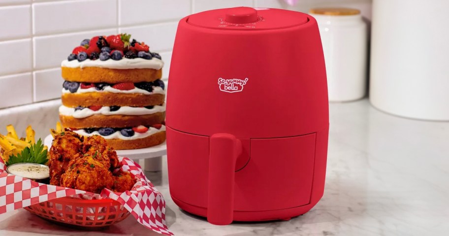 red bella air fryer on counter with wings next to it 