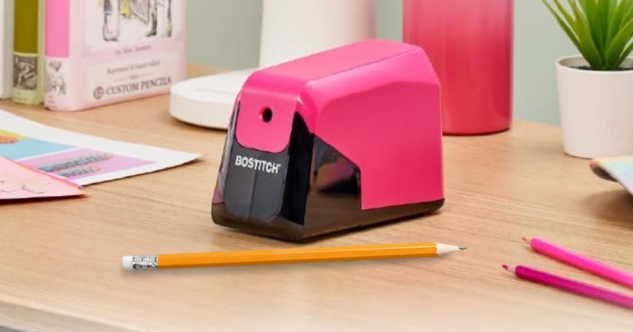 a pink and black pencil sharpener on a desk with pencils around it
