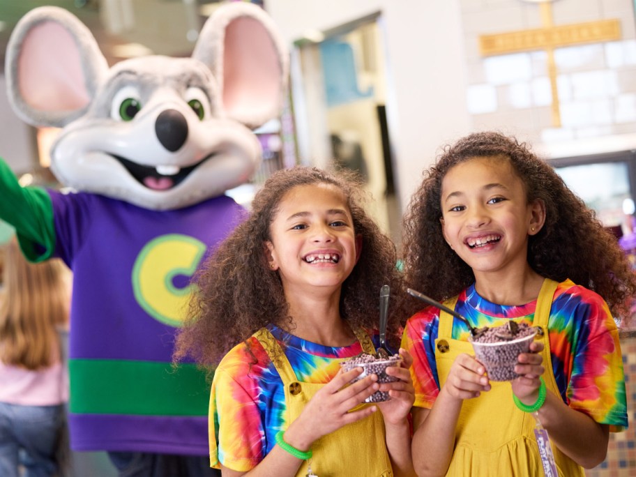 two girls holding cups of dippin dots in front of Chuck E Cheese mascot