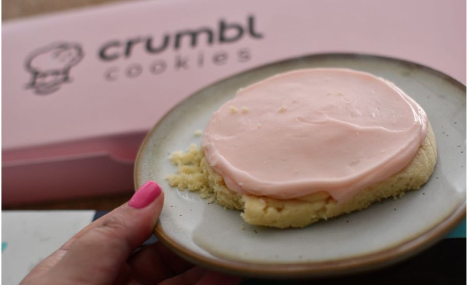 a womans hand holding a plate with a pink crumble cookie on it