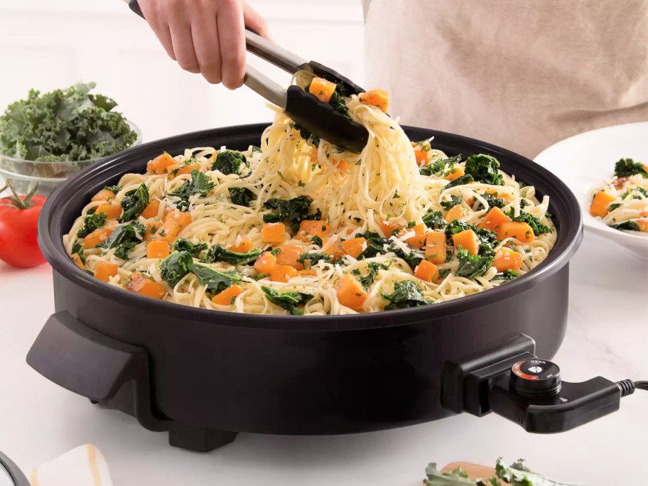 hand using tongs to pull pasta out of a dash skillet