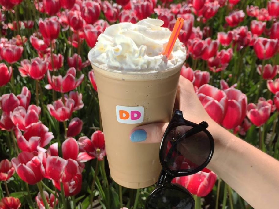 holding a frozen Dunkin beverage in front of flowers