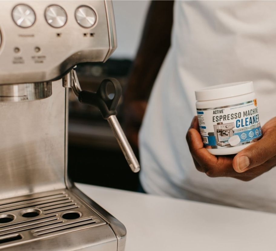 a man holding a jar of espresso cleaner tablets next to an espresso machine 