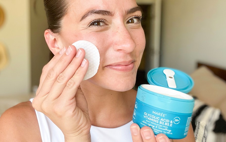 woman using facial pad on face while holding container